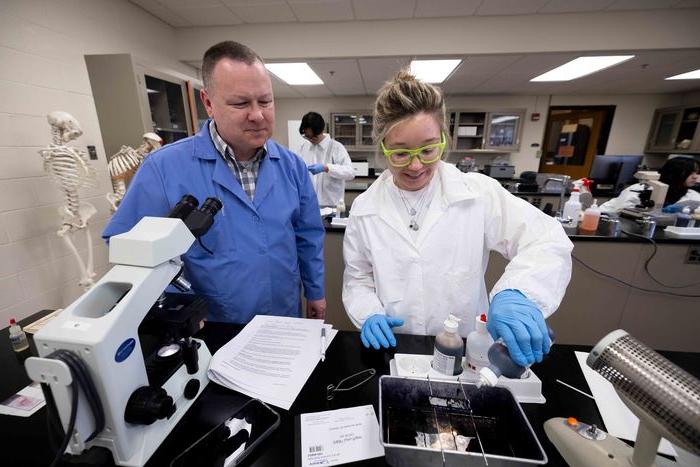 student in lab coat working with their professor